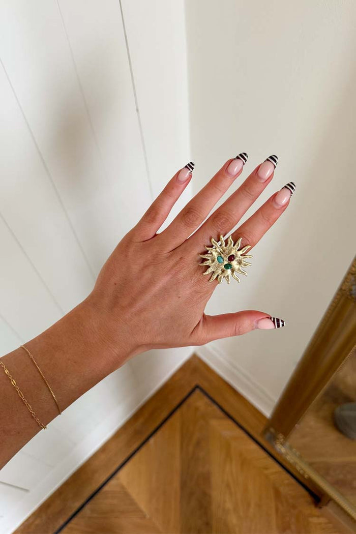 Deloris Sun Ring in brass featuring an iconic sun motif and semi-precious stones, worn on a hand.