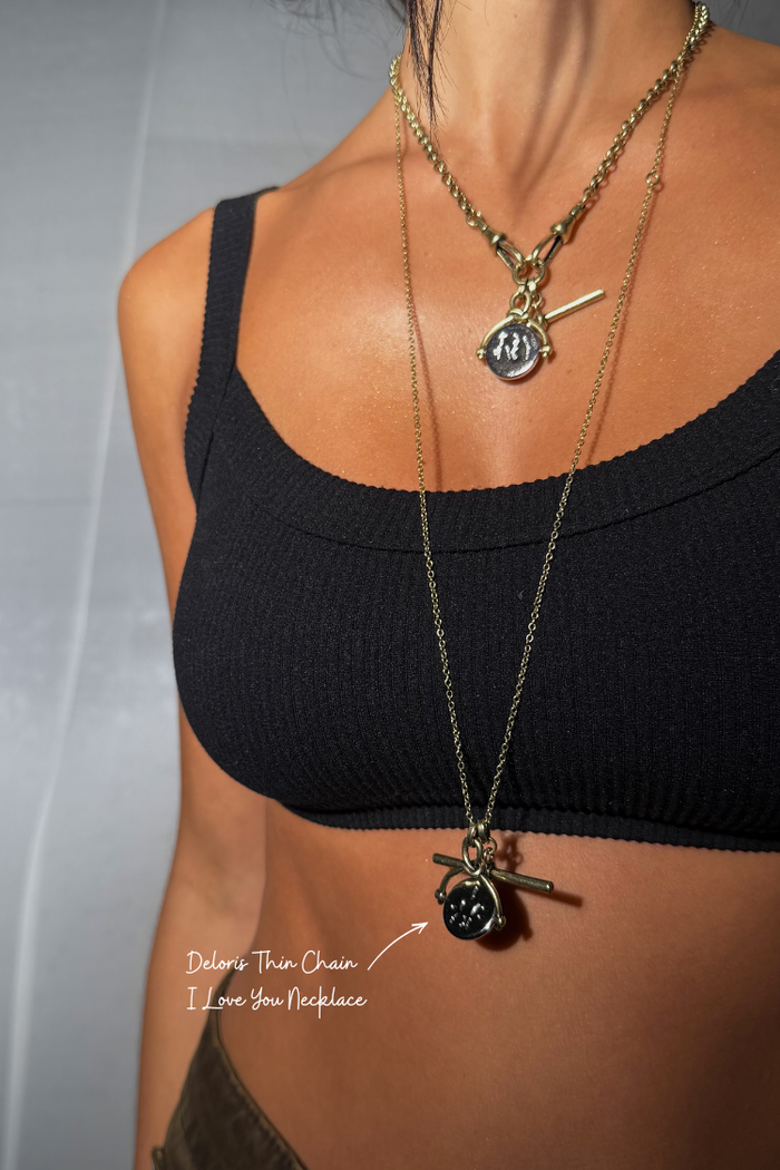 Deloris Thin Chain I Love You Necklace in brass featuring a spinning pendant and lariat drop, layered over a black top.