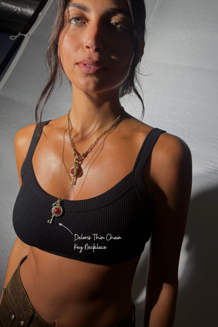 Deloris Thin Chain Key Necklace with a brass key charm and red gemstone, worn by a model.