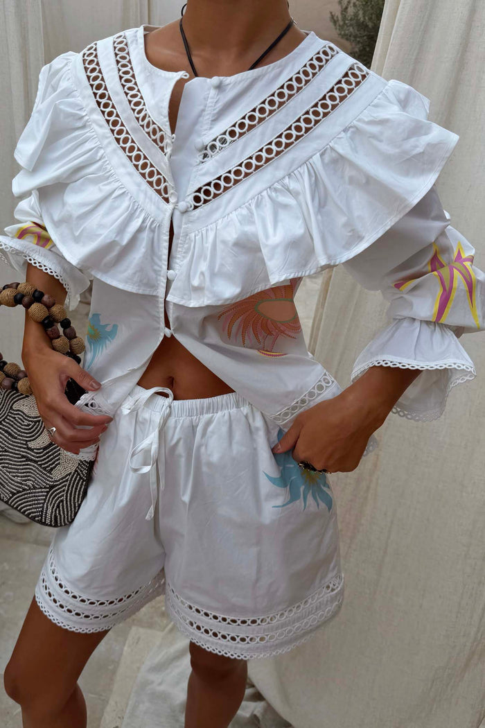 White cotton Dreamer Willa Top featuring sun and star motifs, a ruffled cutout neckline and flared cuffs.