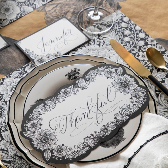 Close-up of an elegant place setting featuring an Ebony Harvest Blooms Table Card with "Thankful" written on it in lovely script resting on the plate.