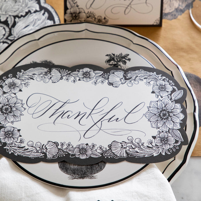 Close-up of an elegant place setting featuring an Ebony Harvest Blooms Table Card with "Thankful" written on it in lovely script resting on the plate.