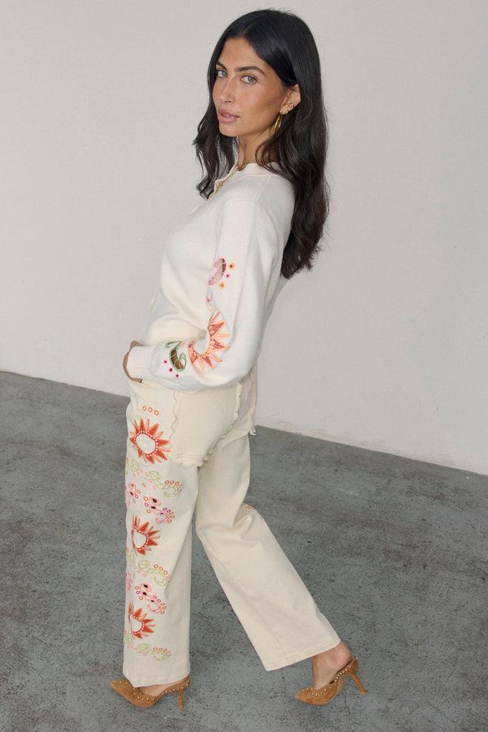 Ecru Enchanted cut-work jeans with colourful sun embroidery and scalloped pockets on a model.