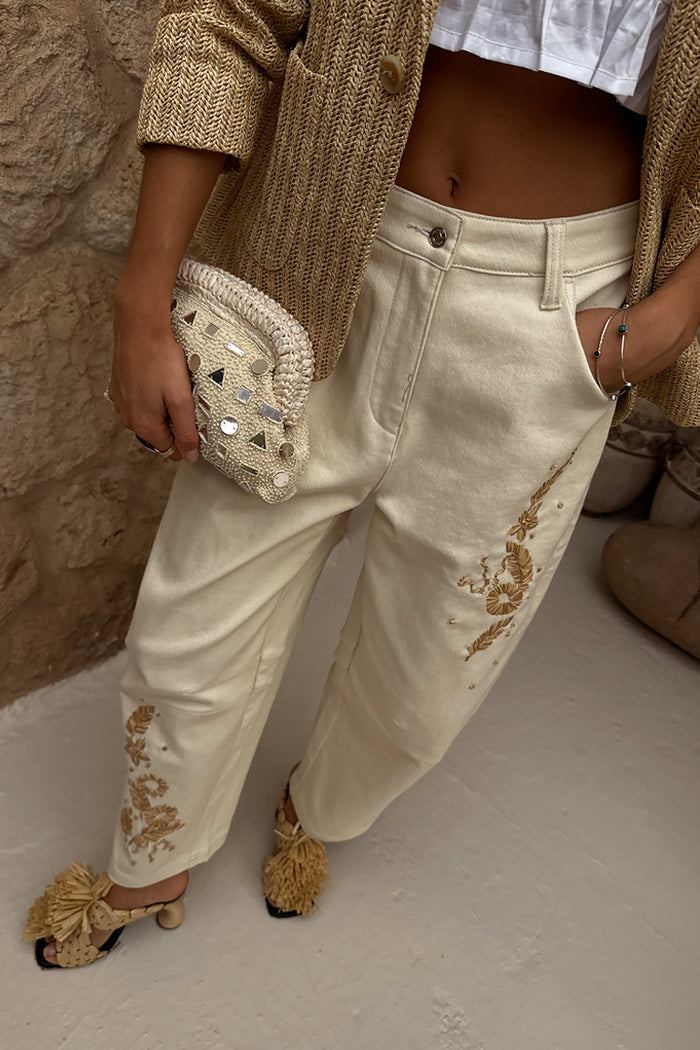 Ecru Raffia Palma Barrel Leg Jeans with palm embroidery, styled with a beige jacket and raffia clutch.