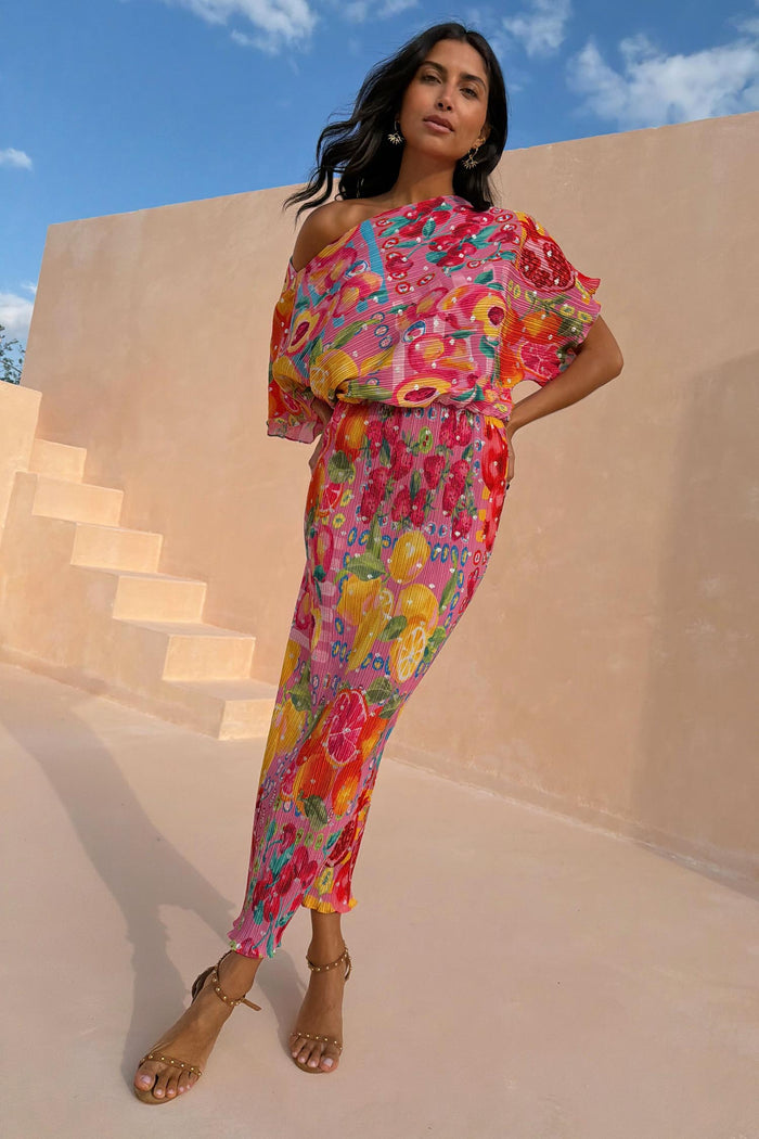 Pink Fruit Tilly midaxi dress with a citrus print, off-shoulder draped top and pleated metallic fabric outdoors.