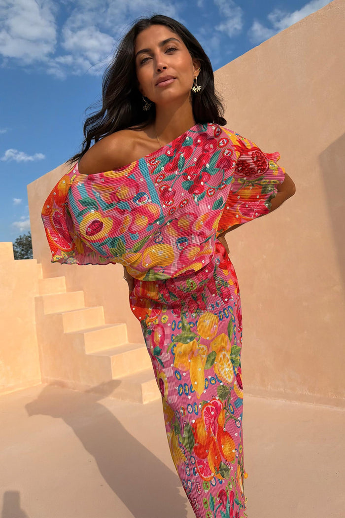 Fruit Tilly Dress in pink with a citrus print, metallic flecks, and an off-shoulder draped top.