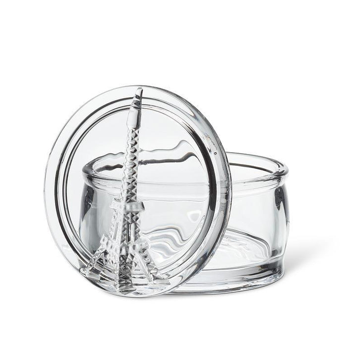 A clear glass round container with a matching glass lid featuring a sculpted Eiffel Tower design, shown on a white background.