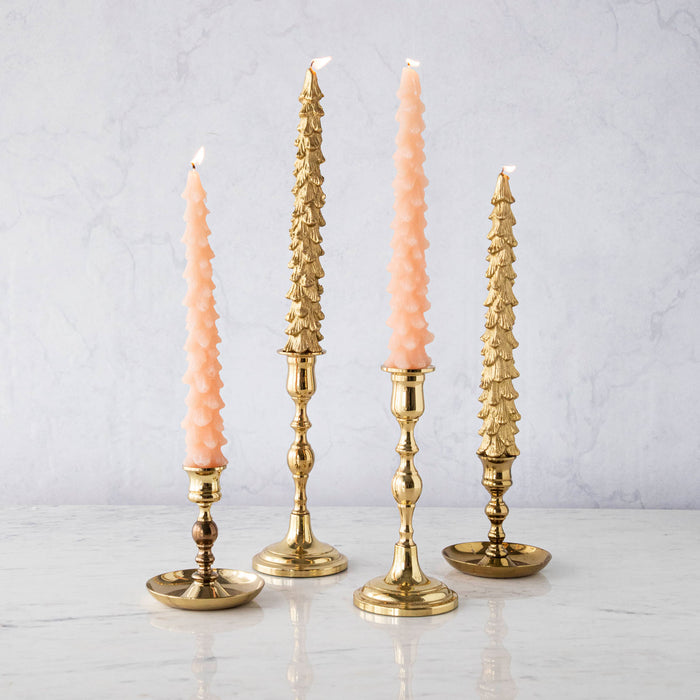 A set of two pink unscented tree-shaped taper candles, with one candle longer than the other, displayed on a surface with a decorative, antique-style gold candle holder.
