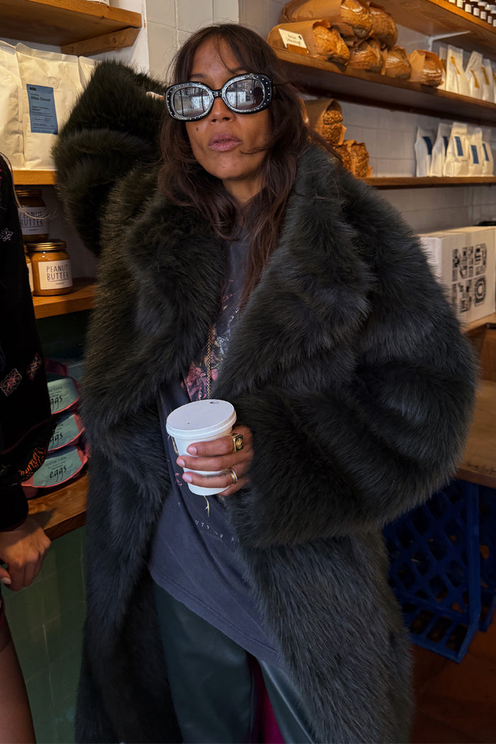 Green Faux Fur Coat with a shaggy texture and relaxed silhouette, styled with sparkly sunglasses in a cafe.