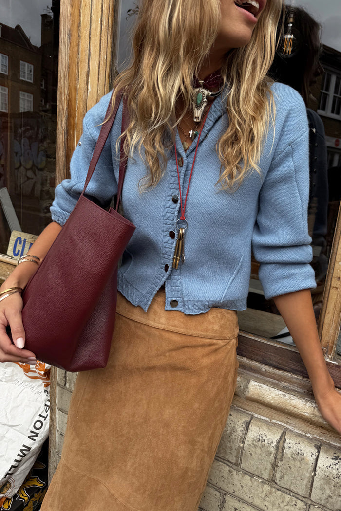 Ice Blue Studded Cardigan with silver metal studs and structured fit, styled with a suede skirt and burgundy bag.