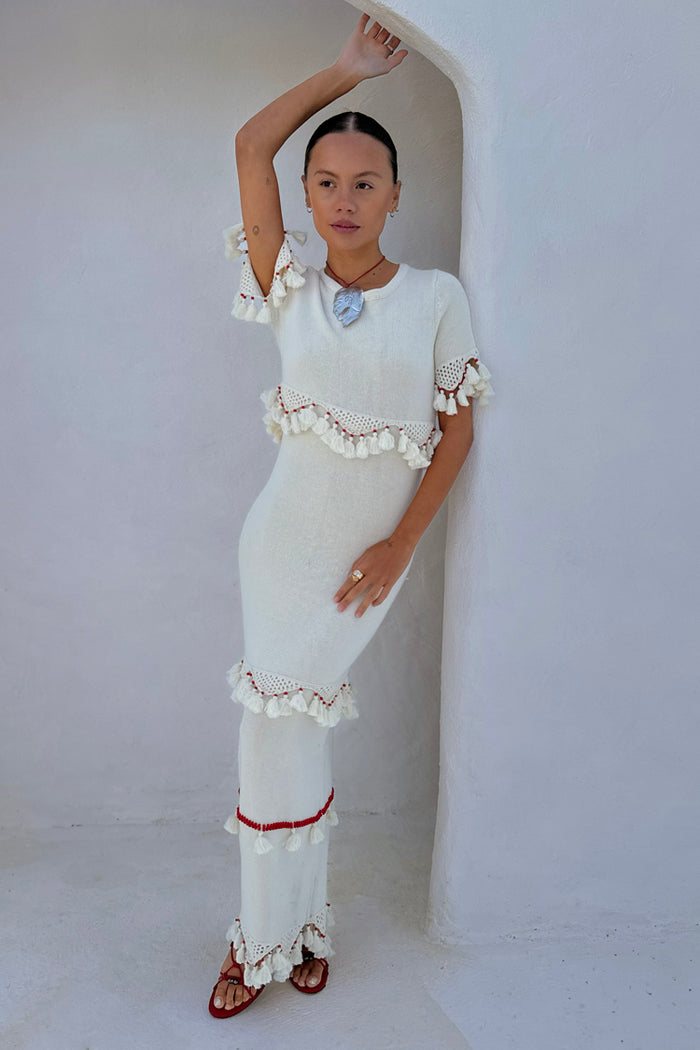 Ivory and Red Harper Dress, a cream knit midaxi with crochet scallop trim and white tassels, styled in a white archway.