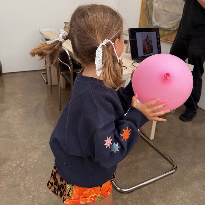Kids Navy Charms Sweatshirt featuring colourful star motifs on the sleeve, worn by a young girl holding a pink balloon.