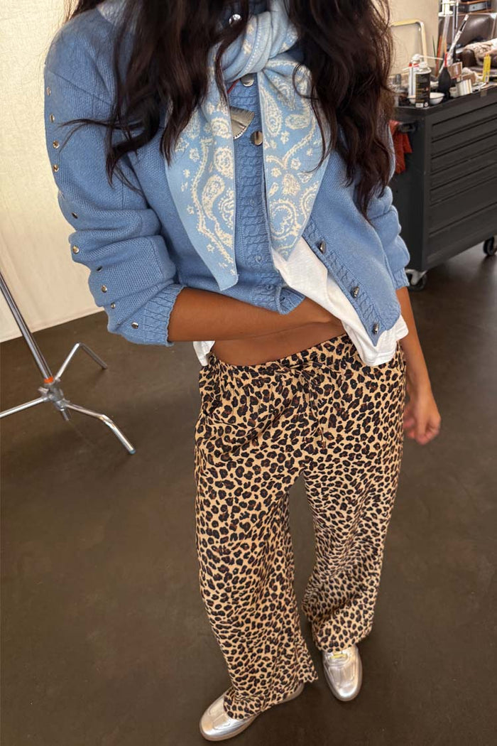 Wide-leg Lucia Leopard Elissa Trousers in leopard print, styled with a blue cardigan and metallic silver sneakers.