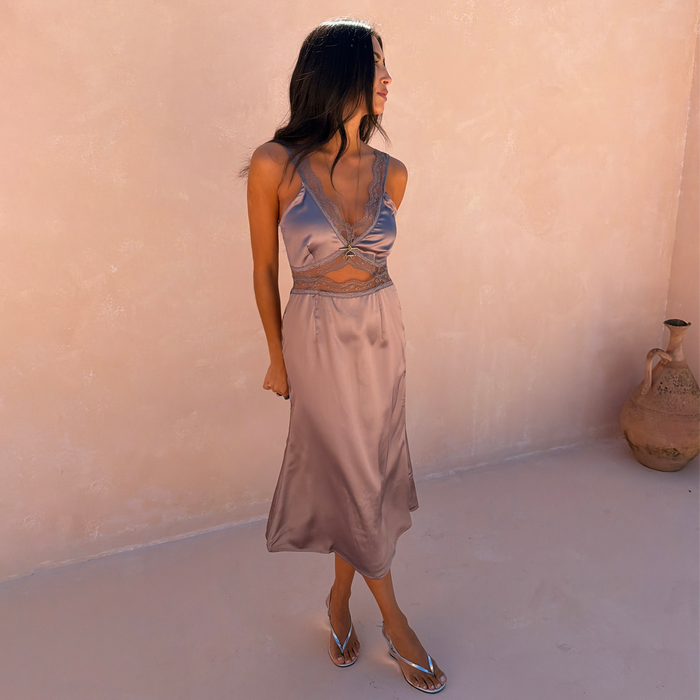 Mink Mimi Dress Petite featuring lace trims and an under-bust cutout, styled with silver sandals against a pink wall.