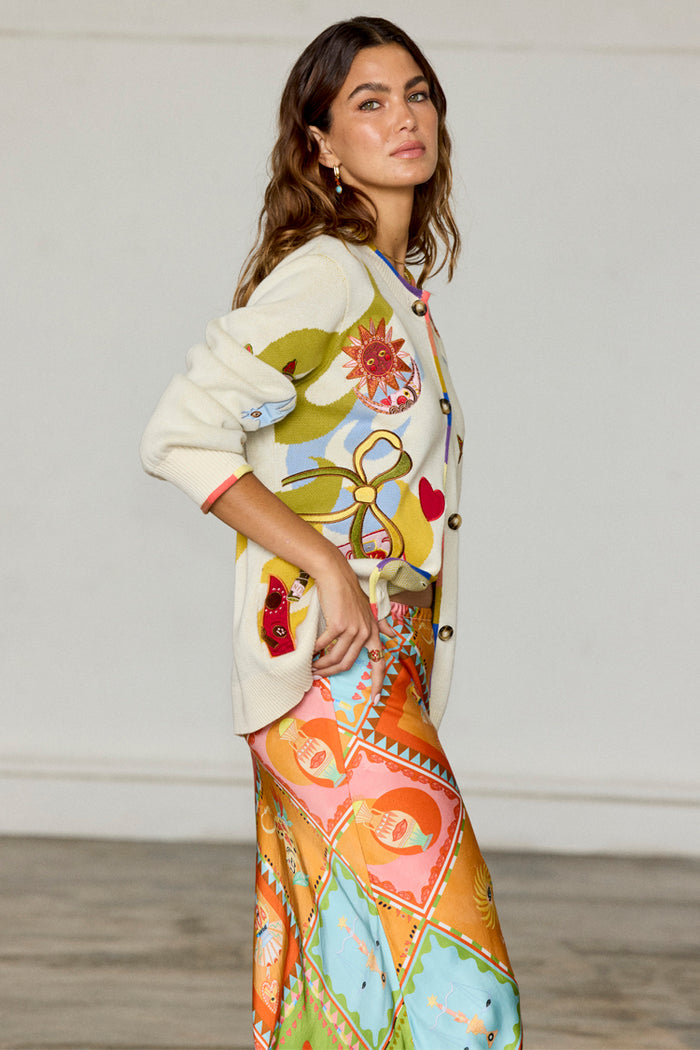 Multi Enchanted Cardigan in cream cotton knit with colourful motifs and ribbed trim, styled with a printed skirt.