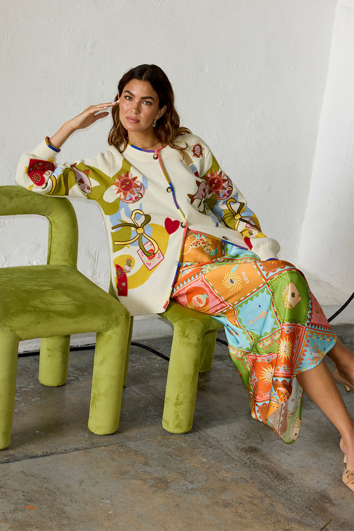 Cream Multi Enchanted Cardigan with illustrative motifs and colourful trim, styled with a printed satin skirt.