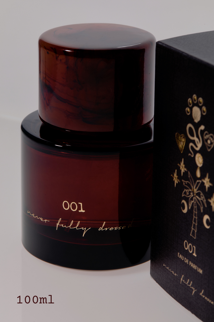 NFD Eau De Parfum 001 in a dark amber bottle with a marbled cap and gold script, beside its black and gold illustrated box.
