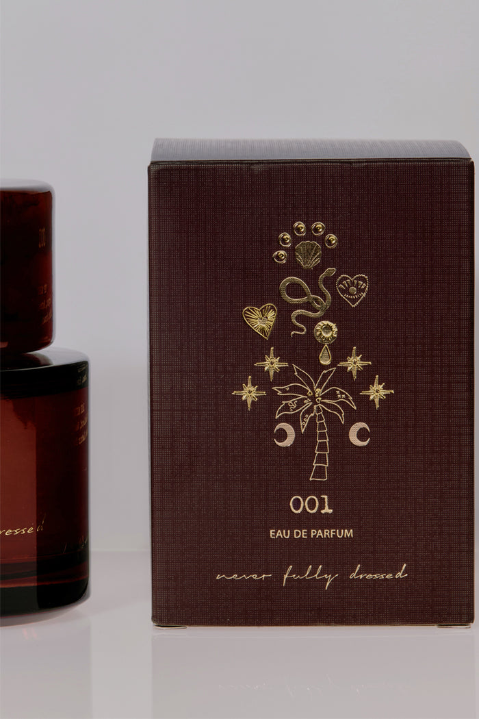 NFD Eau De Parfum 001 burgundy box with gold foil palm tree and star illustrations beside an amber glass bottle.