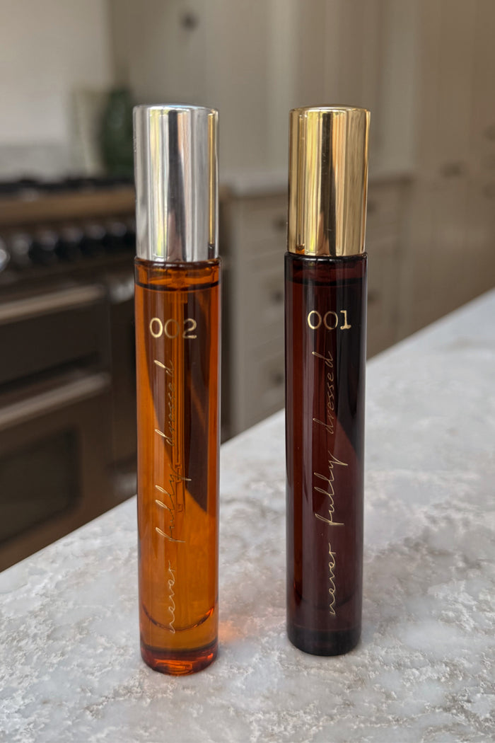 NFD Eau De Parfum 001 and 002 travel spritz bottles in amber glass with silver and gold caps on a marble countertop.