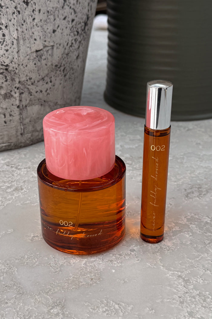 NFD Eau De Parfum 002 amber glass bottle with a marbled pink cap alongside a silver 10ml travel spritz.
