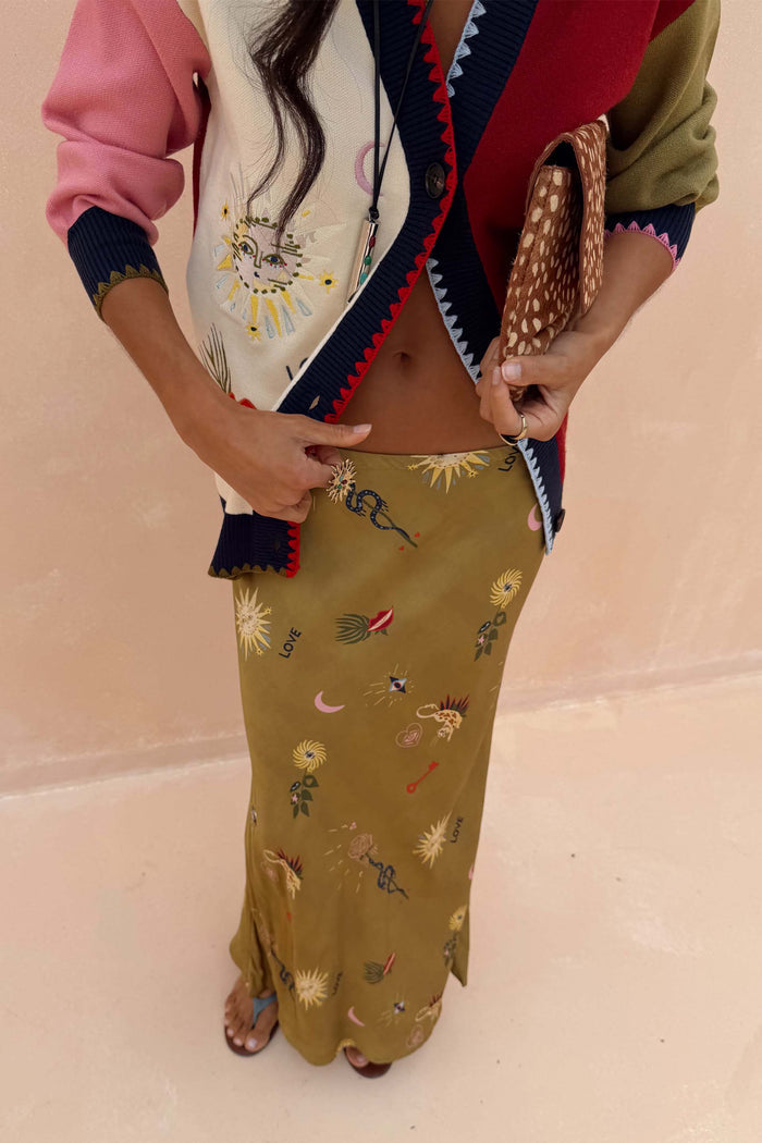 Olive Mystical Dorris Skirt featuring sun and snake motifs, styled with a colour-block cardigan and animal print bag.