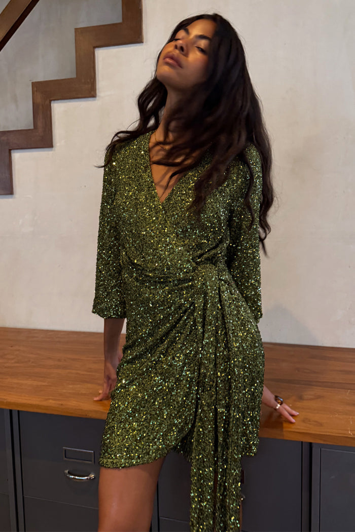 Olive Sequin Mini Vienna Petite dress with green sequins, a wrap front, and multi-wear tie waist, shown on a model.