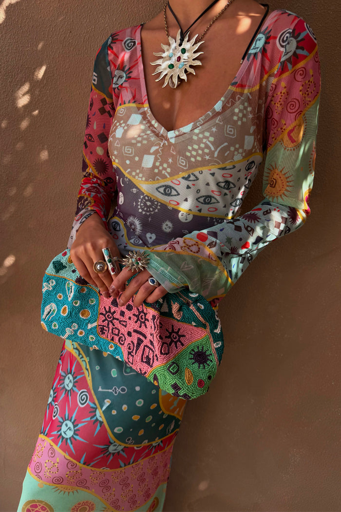 Pastel Morocco Mesh Vivi Dress featuring sun and eye motifs, styled with a beaded clutch and sun necklace.