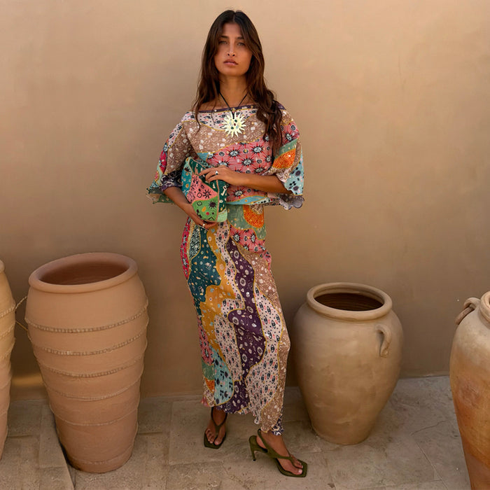 Pastel Morocco Tilly Dress with metallic flecks and sun motifs, styled with a matching clutch beside large clay pots.