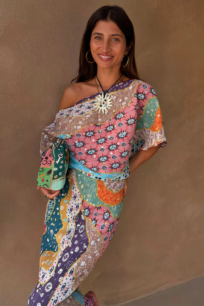Multi-wear Pastel Morocco Tilly Dress featuring metallic flecks and sun motifs, styled off-the-shoulder with a beaded bag.