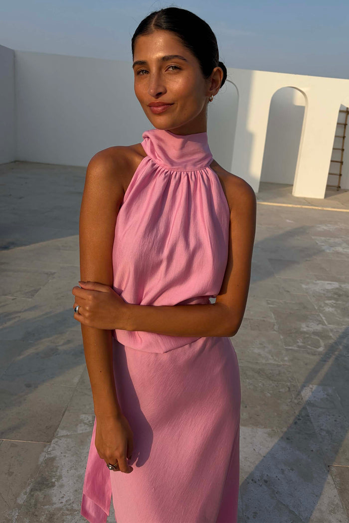 Pink Billie Top featuring a high gathered halterneck and draped fit, styled in an outdoor architectural setting.