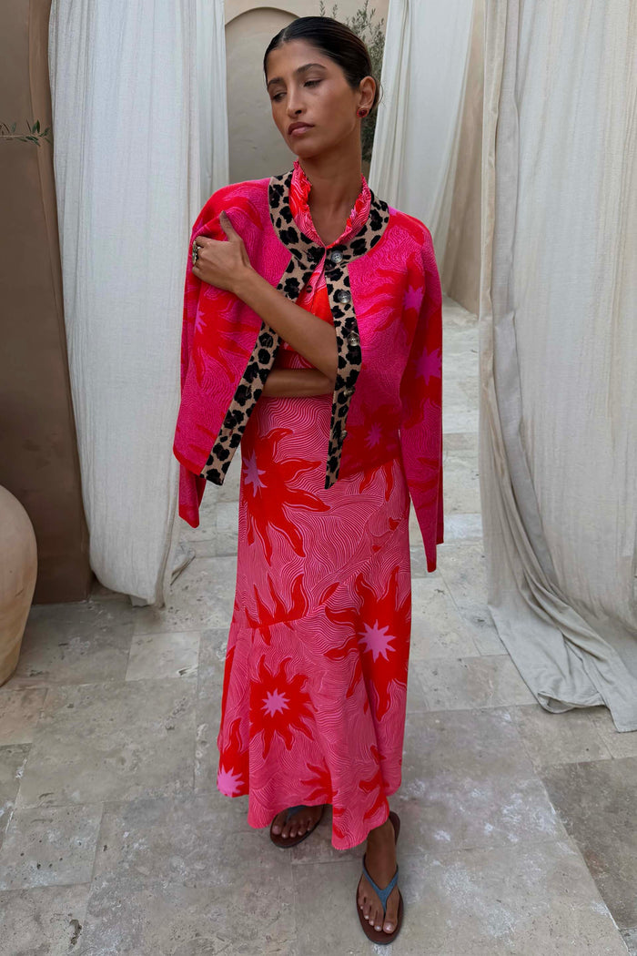 Boxy Pink Soleil knit cardigan with red sun motifs and leopard trim, worn over a matching maxi dress.