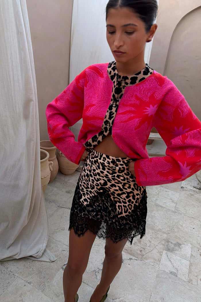 Pink Soleil Cardigan featuring red sun motifs and leopard trim, worn by a 5ft4’’ model in size M with a leopard lace skirt.