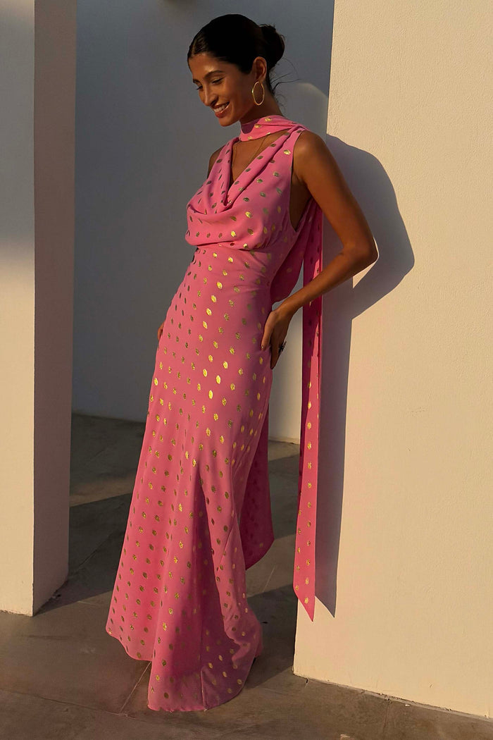 Pink Sophie bias-cut maxi dress with gold fleck and multi-wear scarf on a model leaning against a white pillar.