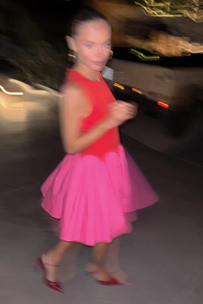 Red and Pink Mini Monika Dress with a corset-style bodice and pleated skirt in a motion-blurred street style shot.