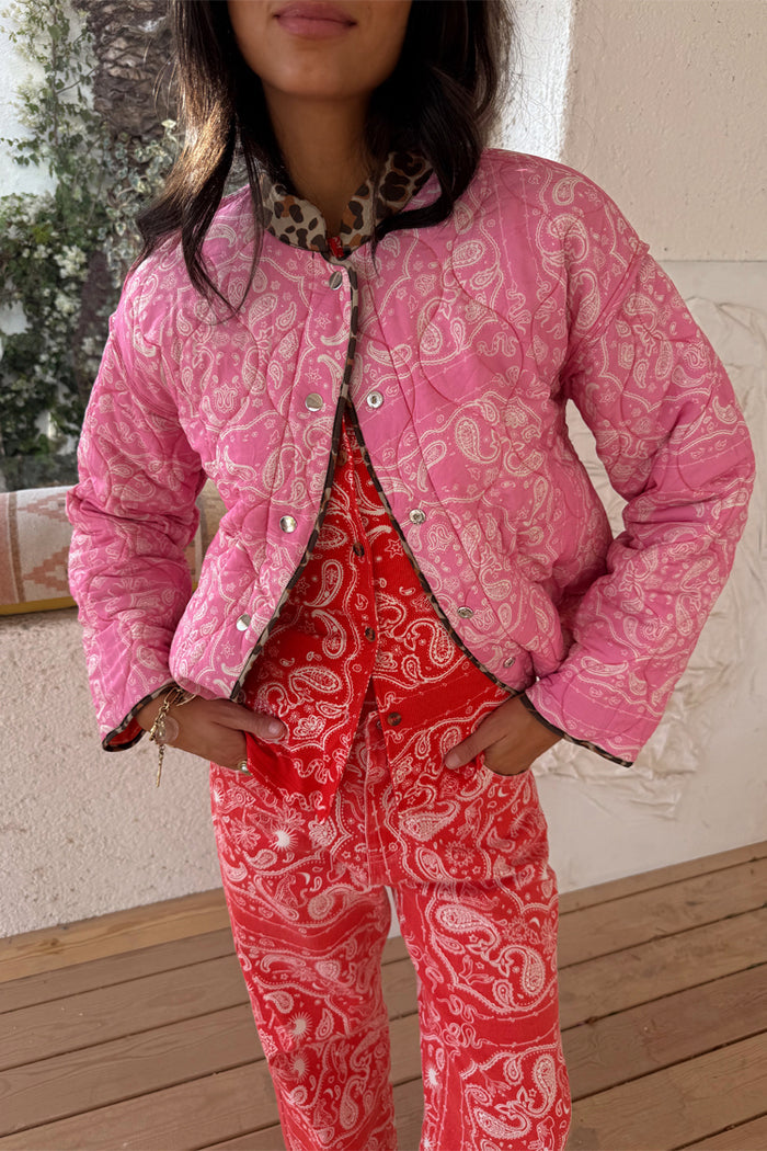 Reversible pink bandana quilted jacket with leopard trim and popper fastenings, styled with matching red trousers.