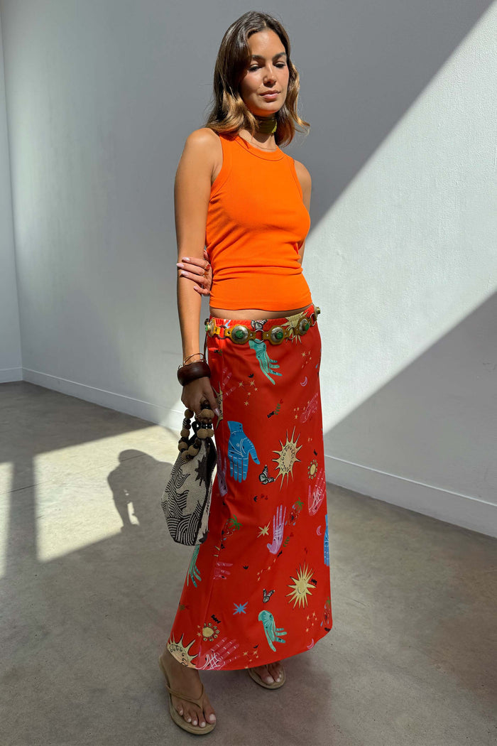 Red Celestial Dorris Satin Skirt with hand-painted motifs, styled with an orange tank top and a patterned bag.