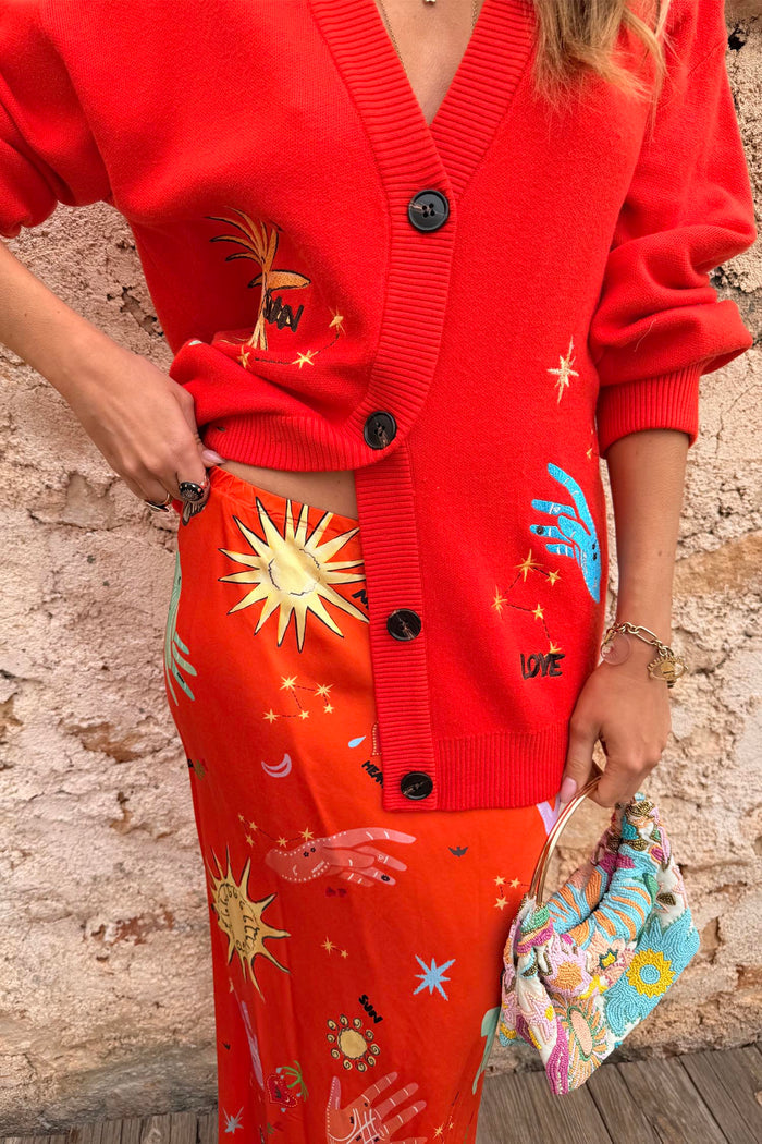 Red Celestial Dorris Skirt in satin with hand-painted sun motifs, styled with a matching red cardigan.