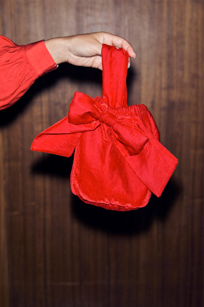 Red Velvet Bow Bag with a large bow detail and elasticated opening, held by a hand.