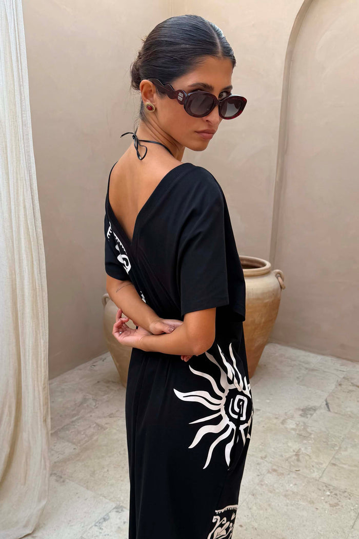Red tortoise acetate sunglasses with wiggle arms and dark lenses, worn by a model in a black sun print dress.