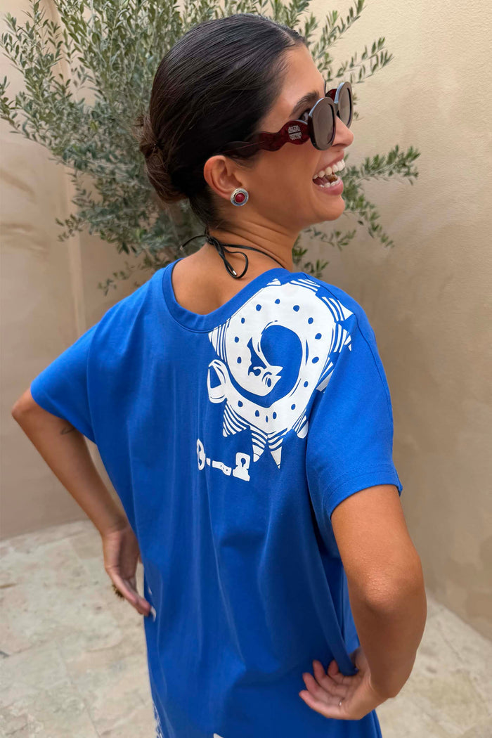 Red Wiggle Arm Acetate Sunglasses with red tortoise frames and dark lenses, worn with a blue graphic t-shirt.