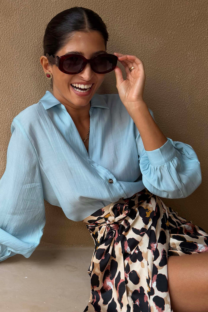 NFD Red Wiggle Arm Acetate Sunglasses in red tortoise with dark lenses, styled with a leopard print skirt on a model.
