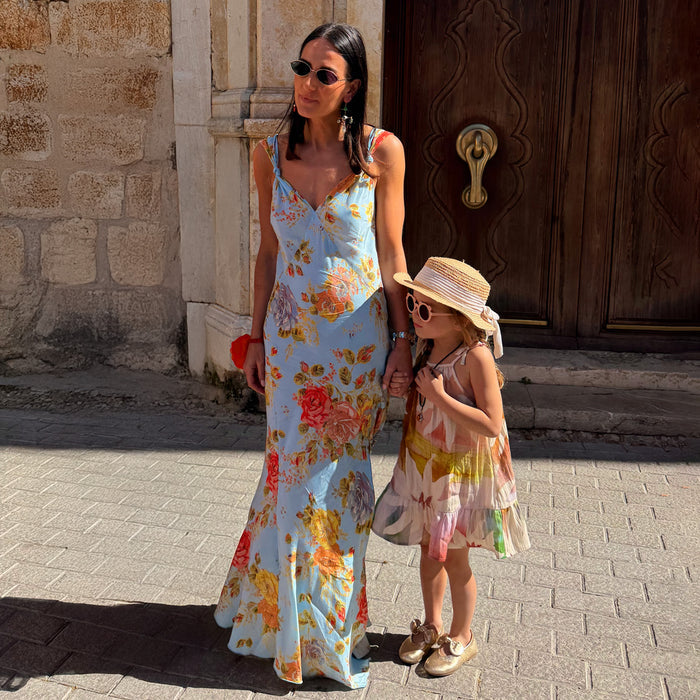 Sky Blue Floral Sofia Dress with tie-knot shoulder straps and a bias-cut drape, worn on vacation with a child.
