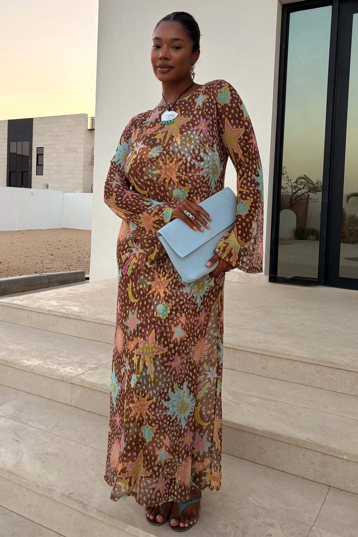 Star Fawn Aria Mesh Dress in brown with celestial star motifs and sheer flared sleeves, worn by a model with a blue clutch.
