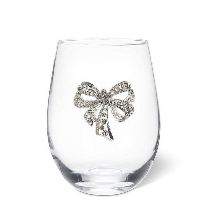 A clear stemless wine glass featuring a decorative silver bow embellished with sparkling clear rhinestones, set against a plain white background.
