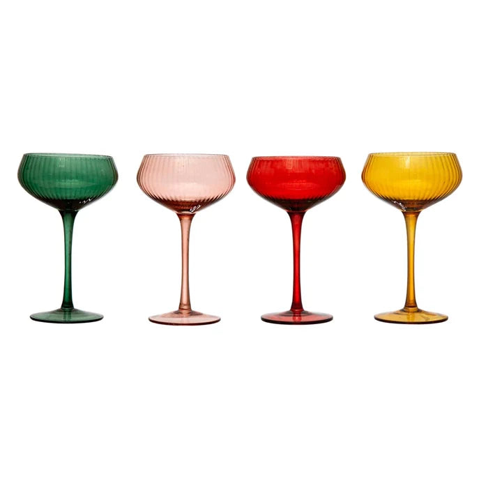 A set of four stemmed champagne coupe glasses in different colors: red, pink, green, and yellow, displayed on a white background.