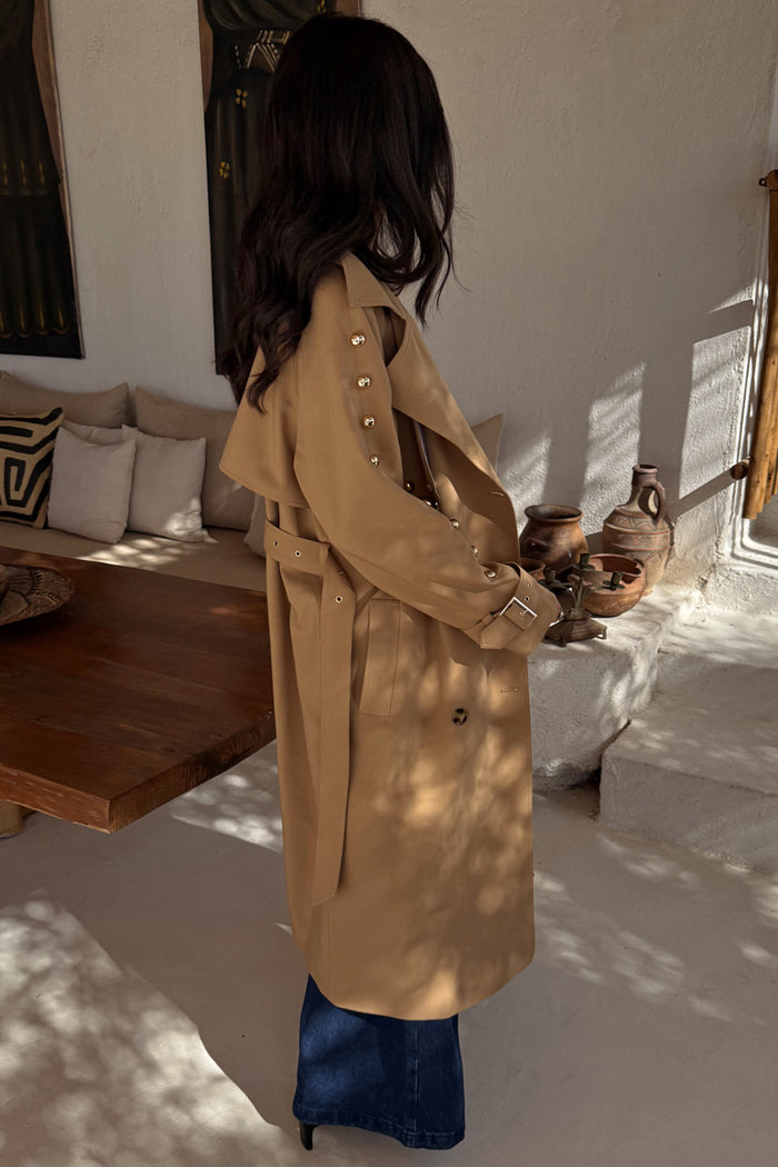 Tan Trench Coat with gold studs on the sleeve and a waist belt, worn by a model who is 5ft7” and wears size M.