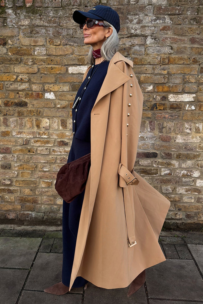 Tan Trench Coat with gold studs on the sleeve, styled with a navy cap and burgundy neck scarf.