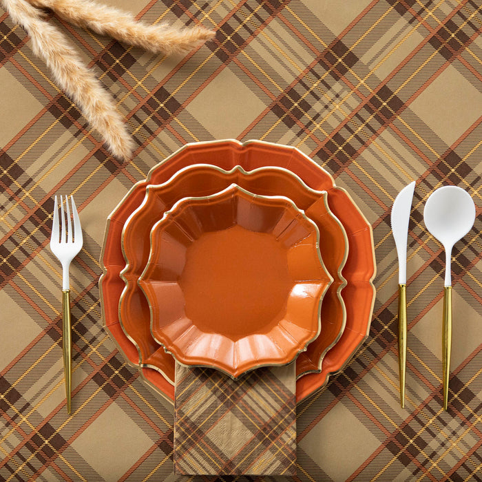 A set of orange scalloped plates with gold rims on a plaid background, accompanied by white utensils with gold accents.