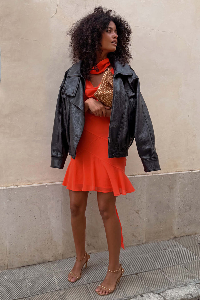 Tomato Mini Sophie Dress in red with a cowl neck and floaty skirt, styled with a black leather jacket and leopard clutch.