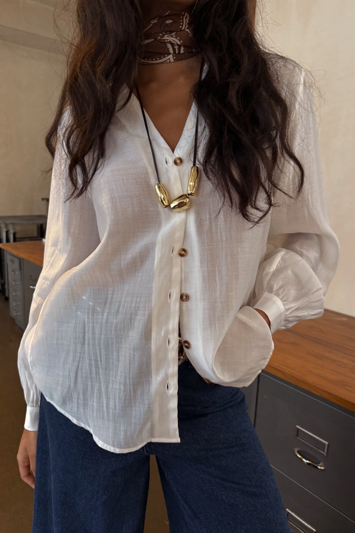 White Miley Shirt with tortoise buttons and blouson sleeves, styled with dark blue jeans and a gold necklace.